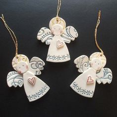 three ceramic angel ornaments hanging from chains on a black surface with gold trimmings