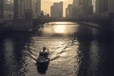 a small boat traveling down a river in the middle of a large city at sunset