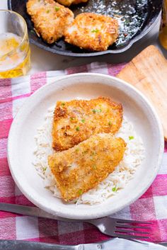 two pieces of fried chicken on top of rice in a bowl next to a skillet