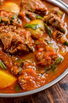 meat and vegetable stew in a bowl on top of a wooden table next to a spoon