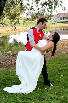 a bride and groom kissing under a tree by the water at their wedding reception in an outdoor setting