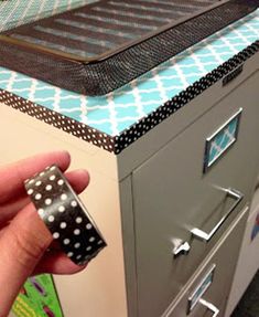 a hand is holding a black and white polka dot cup in front of a filing cabinet