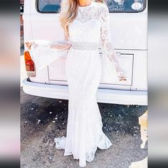 a woman standing in front of a white car wearing a long sleeved wedding dress