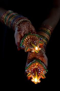 two hands holding lit candles in each other's palms with intricate designs on them