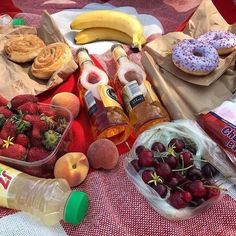 an assortment of fruits and condiments on a picnic blanket with donuts, fruit, juice, and other snacks