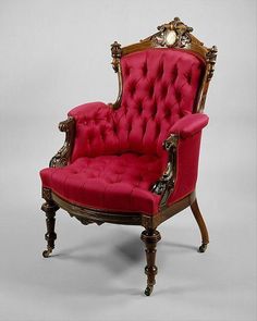 an old fashioned red chair with gold trimmings and buttons on the armrest