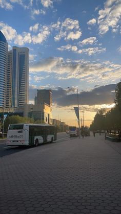 a bus parked on the side of a road next to tall buildings with clouds in the sky