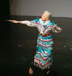 an older woman is performing on stage with her arms spread out to the side,