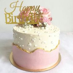 a pink and gold birthday cake with white frosting, flowers and a happy birthday sign on top