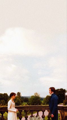 a man and woman standing next to each other in front of a fenced area