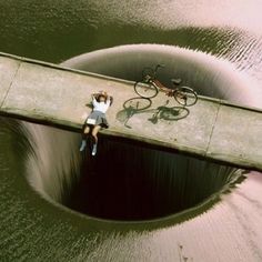 a man laying on top of a large hole in the water next to a bike