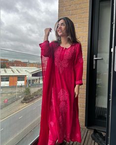 a woman in a red dress is standing on a balcony with her hand up to her face