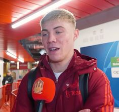 a man in a red jacket is holding a microphone and talking to the camera operator