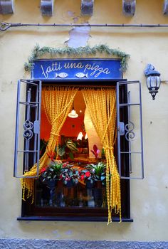 a store front with yellow curtains and flowers in the window