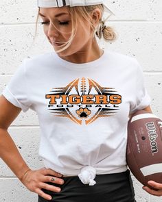 a woman is holding a football and wearing a t - shirt that says tigers on it