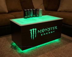 the monster energy drink cooler is lit up with green light and sits on top of a coffee table