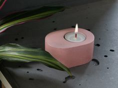 a pink candle sitting on top of a table next to a plant