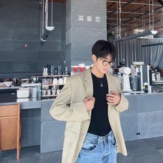 a man standing in front of a counter looking at his cell phone while wearing glasses