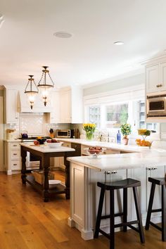 a large kitchen with white cabinets and wood flooring, along with two bar stools