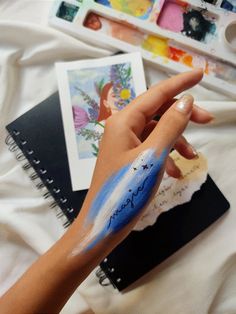 a woman's hand with blue and white paint on her arm next to some art supplies