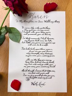 a piece of paper with writing on it next to a red rose and two petals