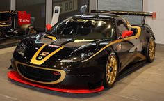 a black and gold sports car on display in a showroom with other cars behind it