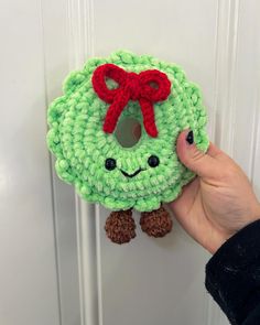 someone is holding up a green crocheted wreath with a red bow on it