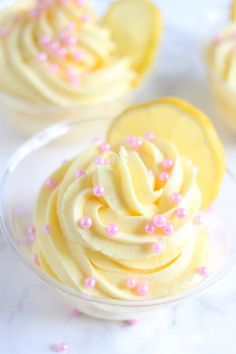 cupcakes with white frosting and pink sprinkles on top in small glass dishes