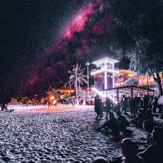 people are sitting on the sand at night with bright lights in the sky above them