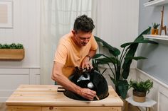 a man in an orange shirt is holding a black helmet on top of a wooden table