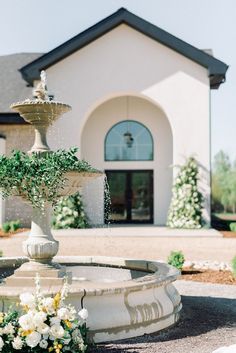 a fountain with flowers in front of a house