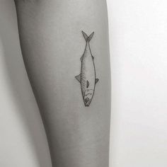 a black and white photo of a fish tattoo on the right thigh, with an outline of a fish