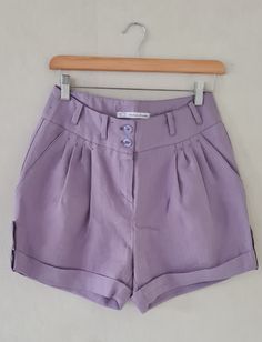 Product description: Short linen trousers with a wide smooth waistband with loops. The short has four pleats and side pockets on both sides. The back has darts. The legs have turn-ups, which are held at the side with a loop and button. Colour: Lilac. Washing advice: Machine wash at 30 degrees. Iron at low temperature. Details: - pleats - cuffs on the legs Compound: 100% ramie linen. Chic Summer Shorts With Button Cuffs, Cotton Bottoms With Pleated Waist In Short Length, Cotton Bottoms With Pleated Waist And Short Length, Pleated Waist Short Workwear Bottoms, Pleated Waist Short Bottoms For Workwear, High-waisted Pleated Summer Pants, Summer High-waisted Pants With Pleated Waist, Summer High-waisted Pleated Waist Pants, Summer Workwear Shorts With Button Cuffs