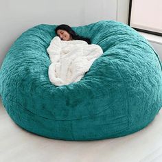 a woman wrapped in a blanket is sitting on a bean bag chair that's shaped like a dog bed