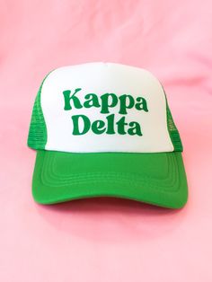 a green and white cap with the words kappa delta on it sitting on a pink background