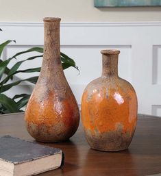 two orange vases sitting on top of a table next to an open book and potted plant