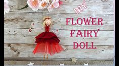 a red fairy doll hanging from the side of a wooden wall with flowers on it