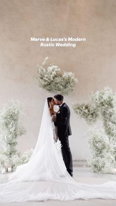 a bride and groom kissing in front of an archway with flowers on the wall behind them