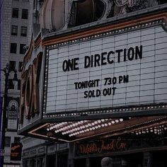 the marquee for one direction theatre is lit up in front of tall buildings