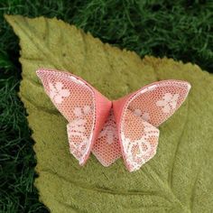 a pink and white butterfly brooch sitting on top of a green leaf in the grass