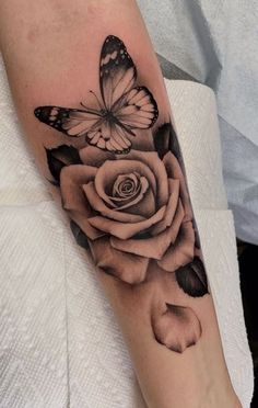 a black and white rose tattoo with a butterfly on it's left arm,