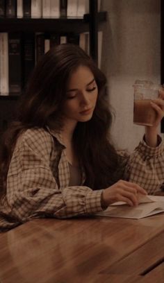 a woman sitting at a table with a book and glass in her hand looking down