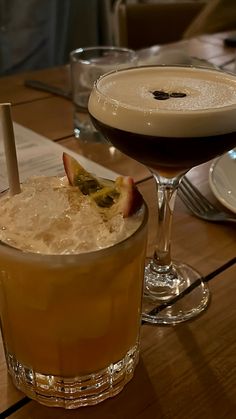 two glasses filled with drinks sitting on top of a wooden table next to plates and utensils