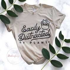 The Perfect Tee For Any Plant Mom, Plant Dad, Or Plant Lover! Makes A Great Gift For Any Occasion! Tee Has Black Graphic That Says, "Easily Distracted By Plants" And A Potted Plant. More Plant Lover Options On Shop.Darlinghoya.Com. Use Code Poshlove For 15% Off Your First Order On My Website! Material, Size, & Care: - 100% Airlume Combed And Ring-Spun Cotton - Sustainably Produced Materials - Screen Print Design - Color: Soft Cream - Unisex - Machine Washable Shipping Carefully Packaged And Ship Tee Ideas, Easily Distracted, Screen Printing Designs, Plant Mom, Plant Lover, Design Color, Black Cream, Screen Print, My Website