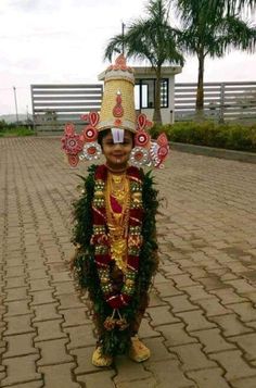 a young boy dressed up in a costume and headdress, standing on a brick walkway