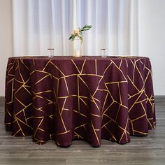 a round table with a purple cloth and gold lines on it, in front of a white curtain