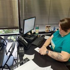 a woman sitting at a desk in front of a computer monitor and keyboard with tattoos on her arm