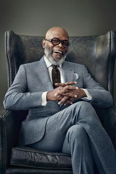 an older man in a suit and tie sitting on a chair with his arms crossed