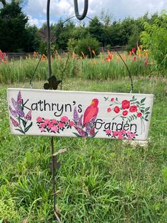 a garden sign in the middle of a field with flowers and birds painted on it