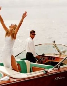 a man and woman on a boat waving to the sky with their arms in the air